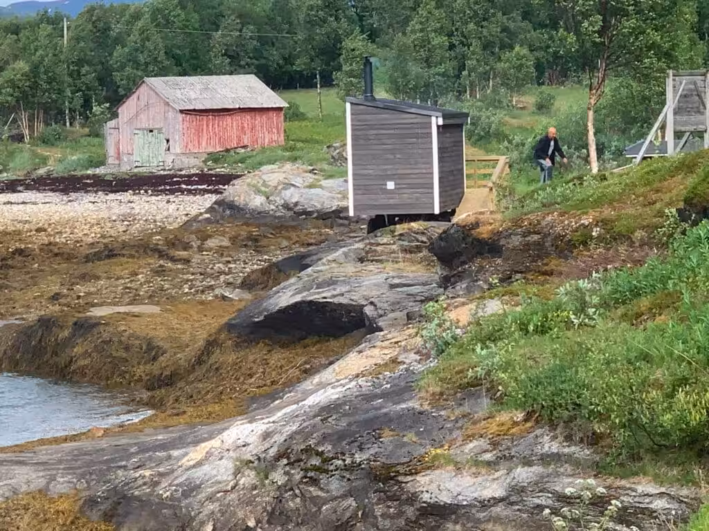 Rolig kystlandskap med svaberg, naust og liten trebygning.
