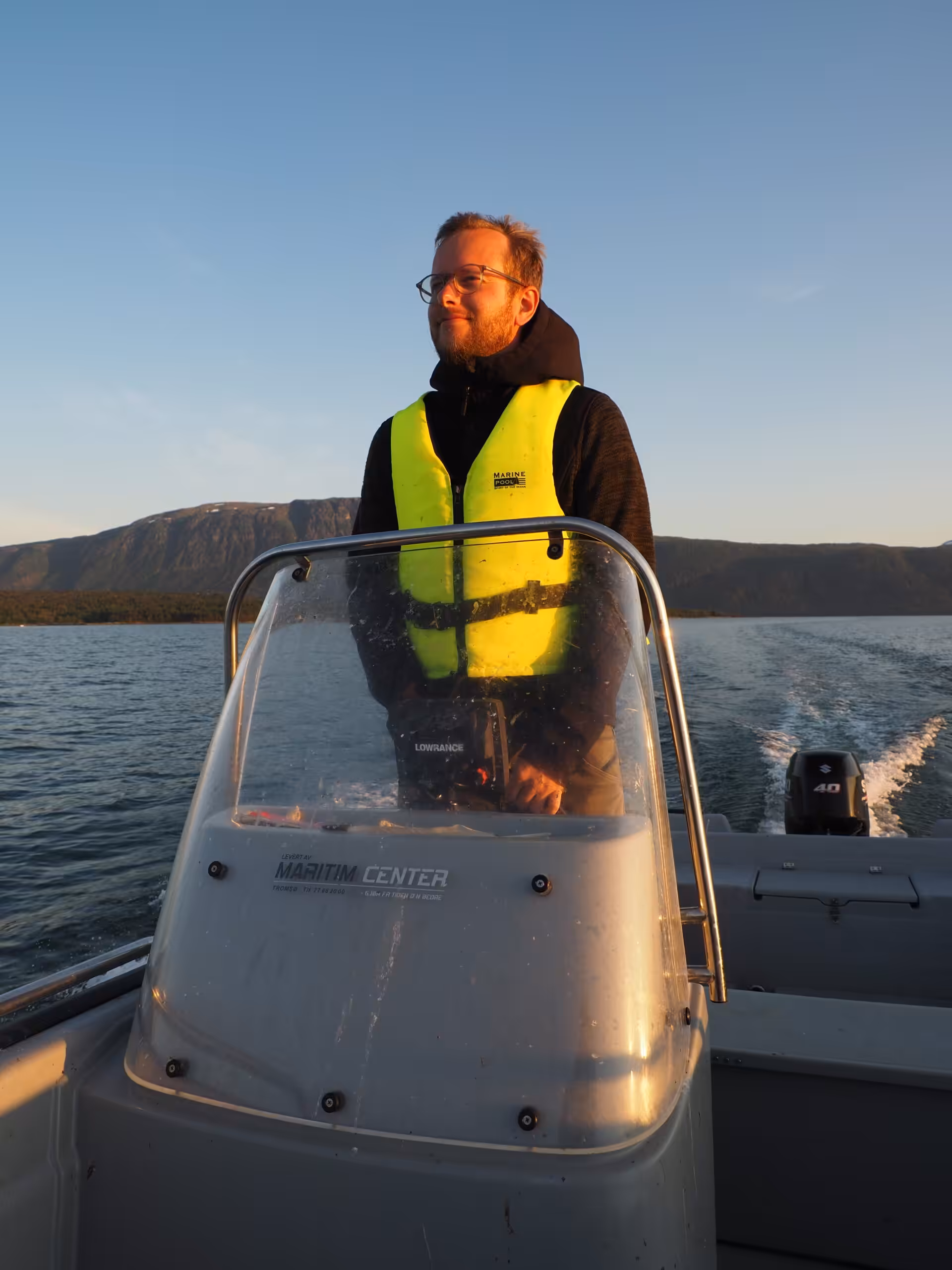 Person am Steuer eines Bootes bei Sonnenuntergang.