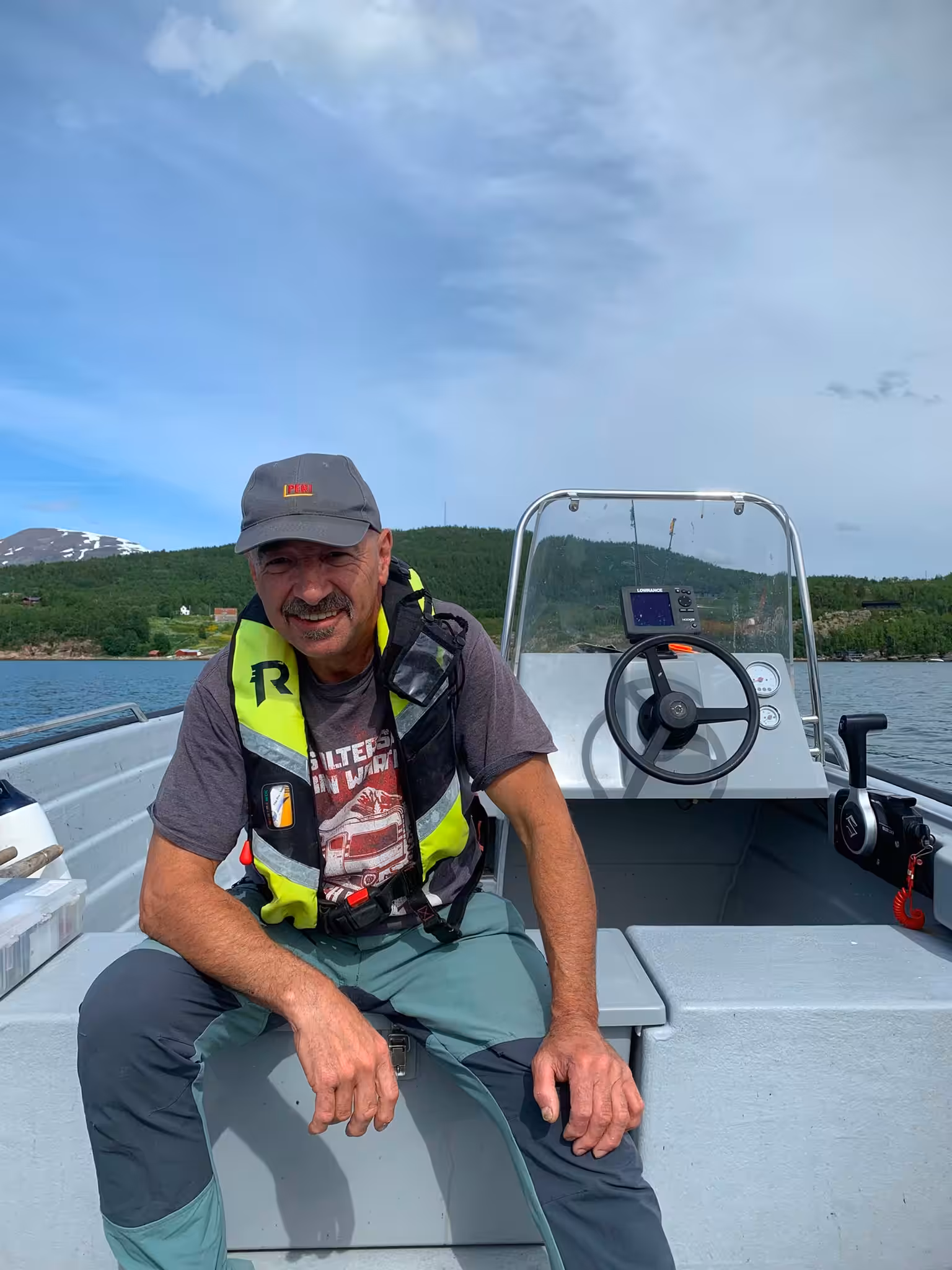 Mann in einem Motorboot auf einem Fjord oder See mit Bergen im Hintergrund